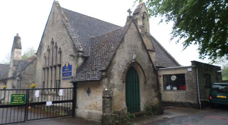 Siddington village school, like most of the older buildings, is old and built from grey stone and has a slate roof. It has a large arched green front entrance door and a gate at the side to allow access to the parking area. It also has a small stone arch on the roof with a bell inset.